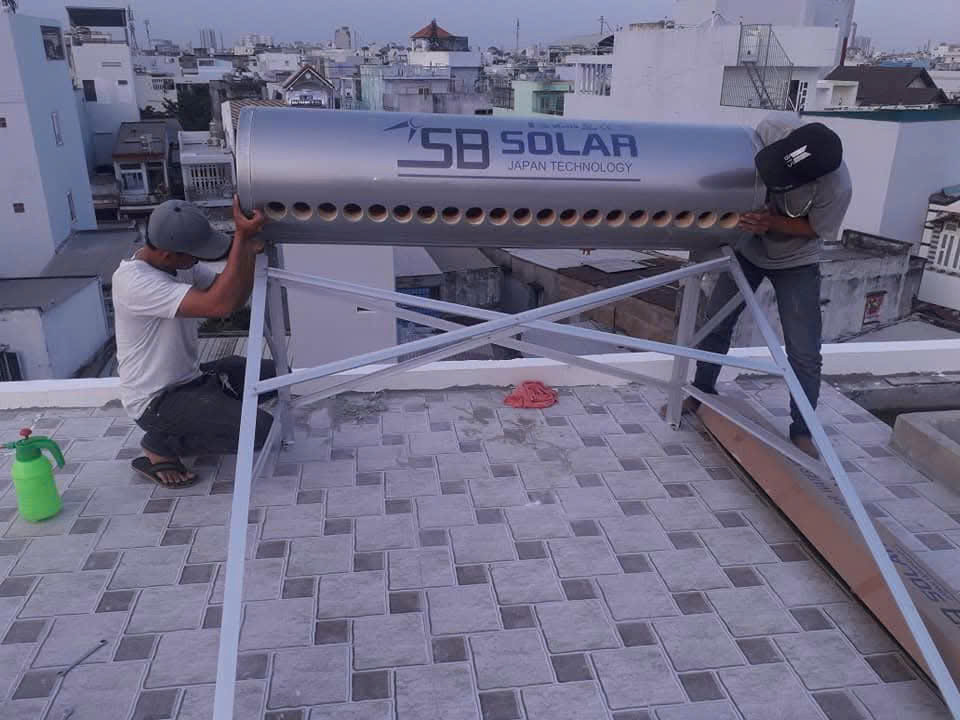 Công trình lắp máy mới: hai kỹ thuật viên đặt bình SB Solar lên khung trên mái, miệng ống chưa lắp dàn thủy tinh.