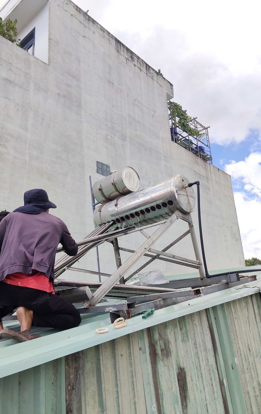 Công trình bảo trì: kỹ thuật viên trên mái, nước chảy từ miệng ống khi tháo / súc bình — không phải hướng dẫn tự làm.